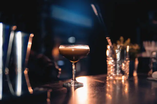 Photo of elegant glass with espresso martini cocktail on blue background;