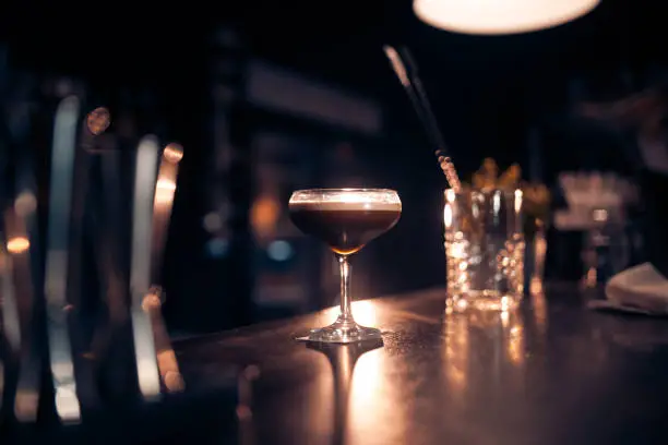 Photo of elegant glass with espresso martini cocktail on blue background;