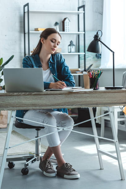 istock focused teenage girl taking notes and using laptop while studying at home 992052192
