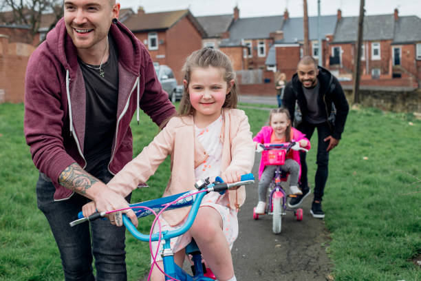Same Sex Male Couple Out With Their Children Young male couple taking their daughters out riding their bicycles in the housing estate gay daddy stock pictures, royalty-free photos & images
