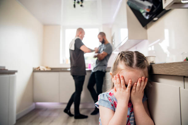 Disagreement in Front of their Child Male couple standing in the kitchen looking to be in disagreement. The focus is on the little girl in the foreground hinding behind her hands. arguing couple divorce family stock pictures, royalty-free photos & images