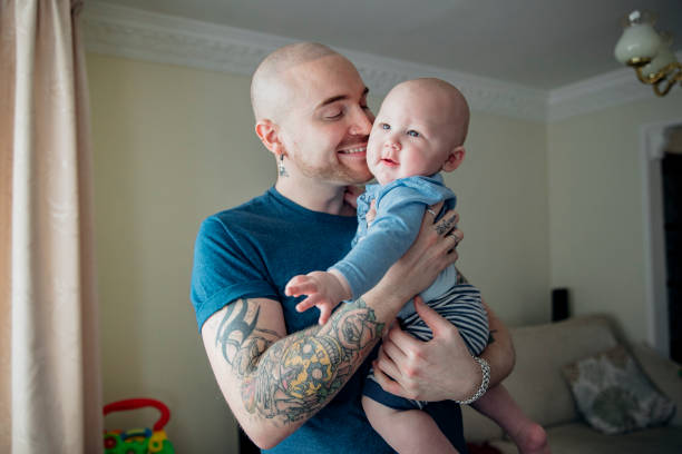 He Loves His Baby Boy Father enjoys being with his young baby boy in the house. They are in the living room as he holds him close and smiles gay daddy stock pictures, royalty-free photos & images