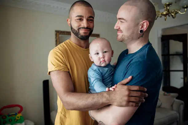 Two men spending time  with their little baby boy. They're all together at home standing in an embrace