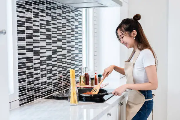 Photo of Asian woman cooking spaghetti in kitchen happily. People and lifestyles concept. Food and drink theme. Interior decoration and housework theme.