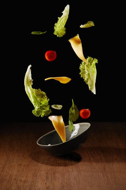 istock Fresh salad with cheese slices and bowl flying above wooden table surface 992083632