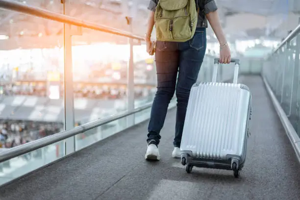 Photo of Close up lower body of woman traveler with luggage suitcase going to around the world by plane. Female tourist on automatic escalator in airport terminal.