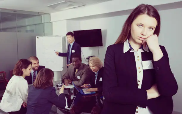 Portrait of unhappy adult woman in boardroom on background with working business colleagues