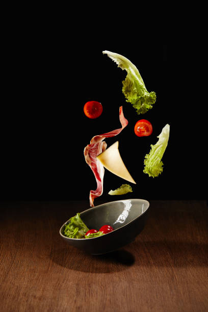 istock Fresh salad with meat and cheese falling in bowl above wooden table surface 992083976