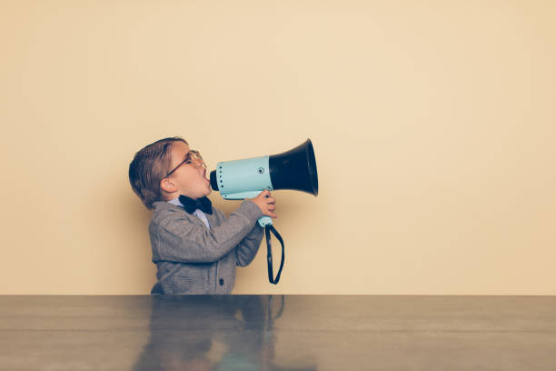 Young Nerd Boy Yells into Megaphone A young nerd boy yells into a megaphone in the studio. He is wearing a bow tie and eyeglasses. He wants you to listen to his important message. announcement message photos stock pictures, royalty-free photos & images