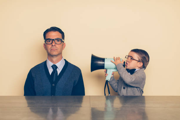 Young Nerd Boy Yelling at Dad through Megaphone A young nerd boy in eyeglasses and a sweater is yelling at his dad with a megaphone. His dad has a blank stare and is ignoring what the son is saying. The son is frustrated with his dad because he won't listen. Parents these days are distracted. relationship difficulties photos stock pictures, royalty-free photos & images