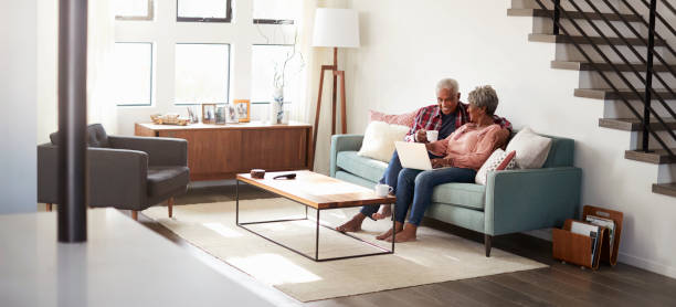 senior pareja sentado en el sofá en casa usando laptop a la tienda en línea - laptop men computer home interior fotografías e imágenes de stock