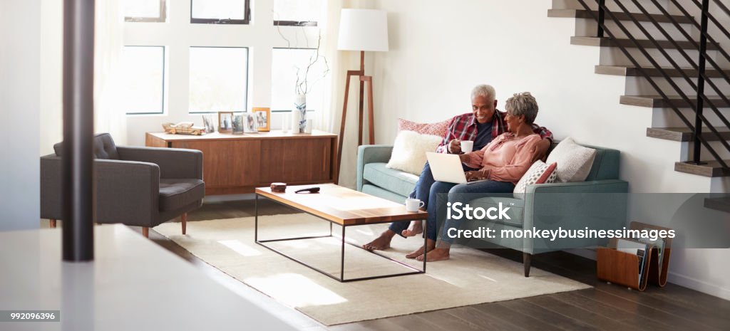 Casal senior sentado no sofá em casa usando o Laptop para fazer compras on-line - Foto de stock de Terceira idade royalty-free