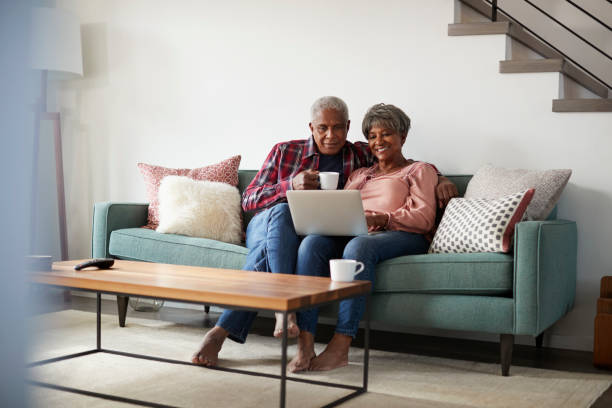 senior pareja sentado en el sofá en casa usando laptop a la tienda en línea - couple home interior laptop computer fotografías e imágenes de stock