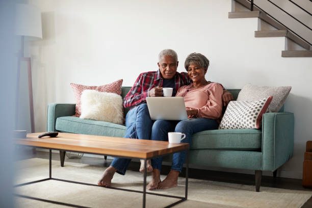資深夫婦坐在沙發上, 在家裡使用筆記本電腦線上購物 - 銀髮族網民 個照片及圖片檔