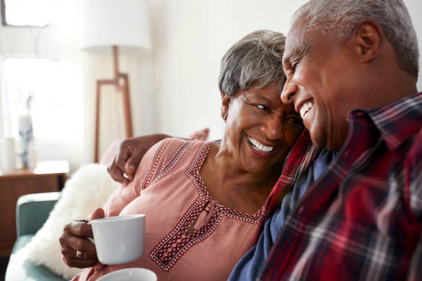 amorosa pareja senior sentado en el sofá en casa relax con bebida caliente - retirement living fotografías e imágenes de stock