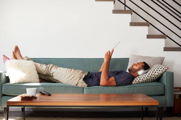 homme allongé sur le canapé à la maison de casque et de regarder des films sur tablette numérique - être étendu photos et images de collection