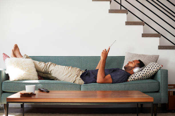 o homem deitado no sofá em casa usando fones de ouvido e assistir filme em digital tablet - men home interior house entertainment - fotografias e filmes do acervo