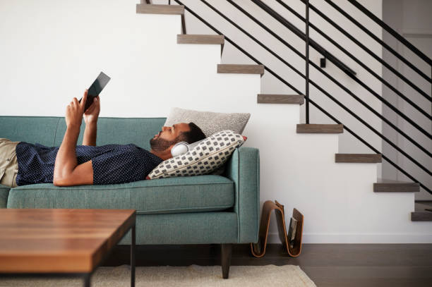 homme allongé sur le canapé à la maison de casque et de regarder des films sur tablette numérique - lying on side audio photos et images de collection