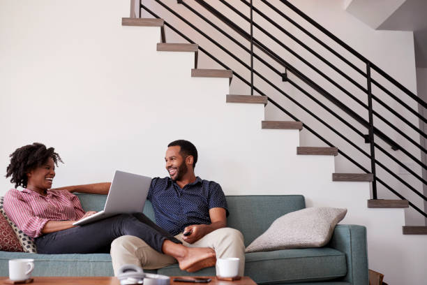 Couple Sitting On Sofa At Home With Woman Using Laptop Computer