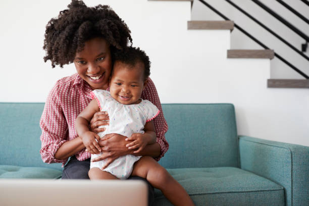 istock Mother With Baby Daughter Sitting On Sofa At Home Looking At Laptop Computer 992100668