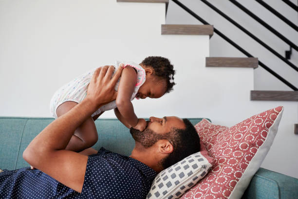 istock Father Lying On Sofa At Home Lifting Baby Daughter Into Air 992101356