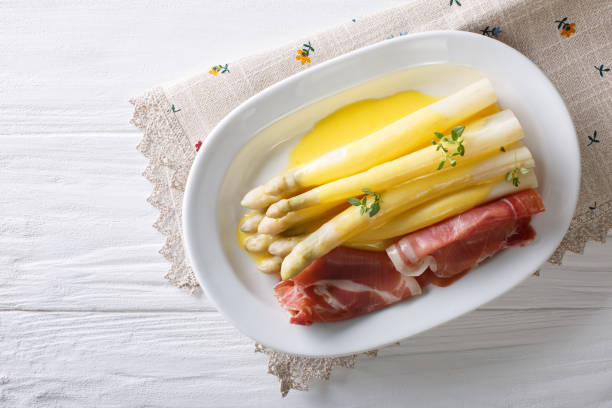 white asparagus with hollandaise sauce and ham close-up on a plate. horizontal top view - hollandaise sauce imagens e fotografias de stock