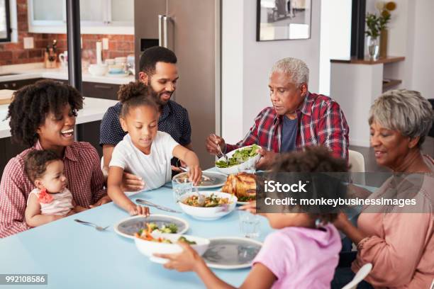 Famiglia Multigenerazionale Che Si Gode Il Pasto Intorno Al Tavolo A Casa - Fotografie stock e altre immagini di Famiglia