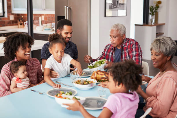 Multi Generation Family Enjoying Meal Around Table At Home Multi Generation Family Enjoying Meal Around Table At Home black people eating stock pictures, royalty-free photos & images