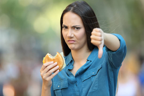 Woman refusing a burger with thumbs down Front view portrait of an angry woman refusing a burger with thumbs down on the street spanish hamburger stock pictures, royalty-free photos & images
