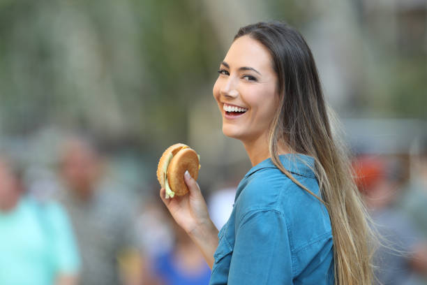 Happy woman holding a burger looking at you Happy woman holding a burger looking at you on the street spanish hamburger stock pictures, royalty-free photos & images
