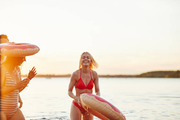 смеющаяся молодая женщина веселится с друзьями на озере - inner tube swimming lake water стоковые фото и изображения