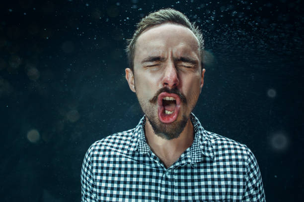Young handsome man with beard sneezing, studio portrait Young funny handsome man with beard and mustache sneezing with spray and small drops, studio portrait on black background. Comic, caricature, humor. illness, infection, ache. Health concept sneezing photos stock pictures, royalty-free photos & images