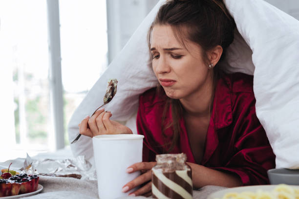 istock Stressed woman hiding under coverlet eating ice cream 992134358