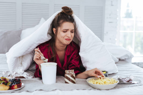 istock Crying woman lying in her bed surrounding by snacks 992134402