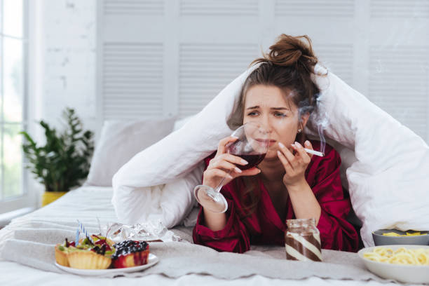 istock Heartbroken woman smoking while lying in bed drinking wine 992135564
