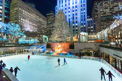 New York City, New York/United States - January 7, 2015: Brightly illuminated the Rockefeller Plaza ice skating rink filled with tourists and locals skating and watching, with a Christmas tree during the holiday season.