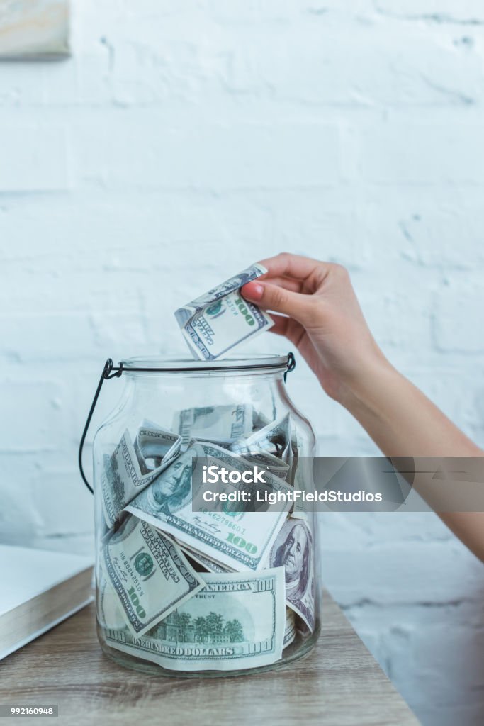 cropped view of female hand putting dollar banknote into glass jar Savings Stock Photo