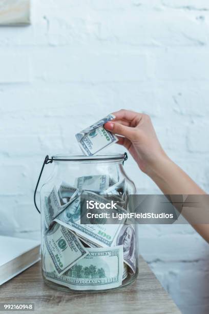 Cropped View Of Female Hand Putting Dollar Banknote Into Glass Jar Stock Photo - Download Image Now
