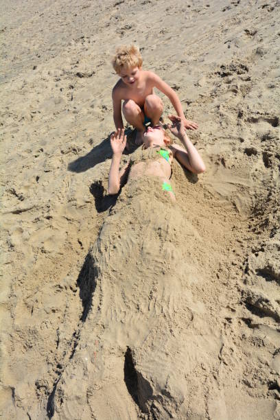 istock Girl in the sand dug and boy sits besides 992254324