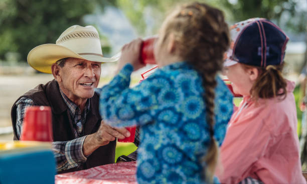 A hungry rodeo family sharing a meal of pizza after a long day of riding, roping, and fun.  Outdoors at picnic tables.