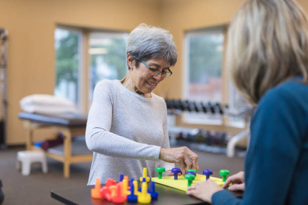 Occupational therapist works with an elderly woman An occupational therapist works with a senior Caucasian woman They are seated at a table and they are doing a fun exercise that involves putting pegs into a plastic board. occupational therapy photos stock pictures, royalty-free photos & images
