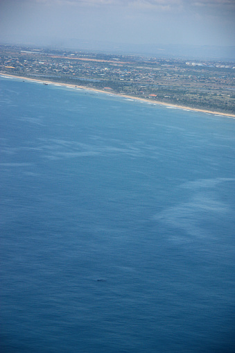Whale watching from the airplane in Ghana. Every year, for around two weeks, humpback whale mothers are bringing their babies to the warmer water off the shore of Ghana to feed them. Shoreline, fisherboats (long boats) and a village on the land is visible as well, while the whale dives again.