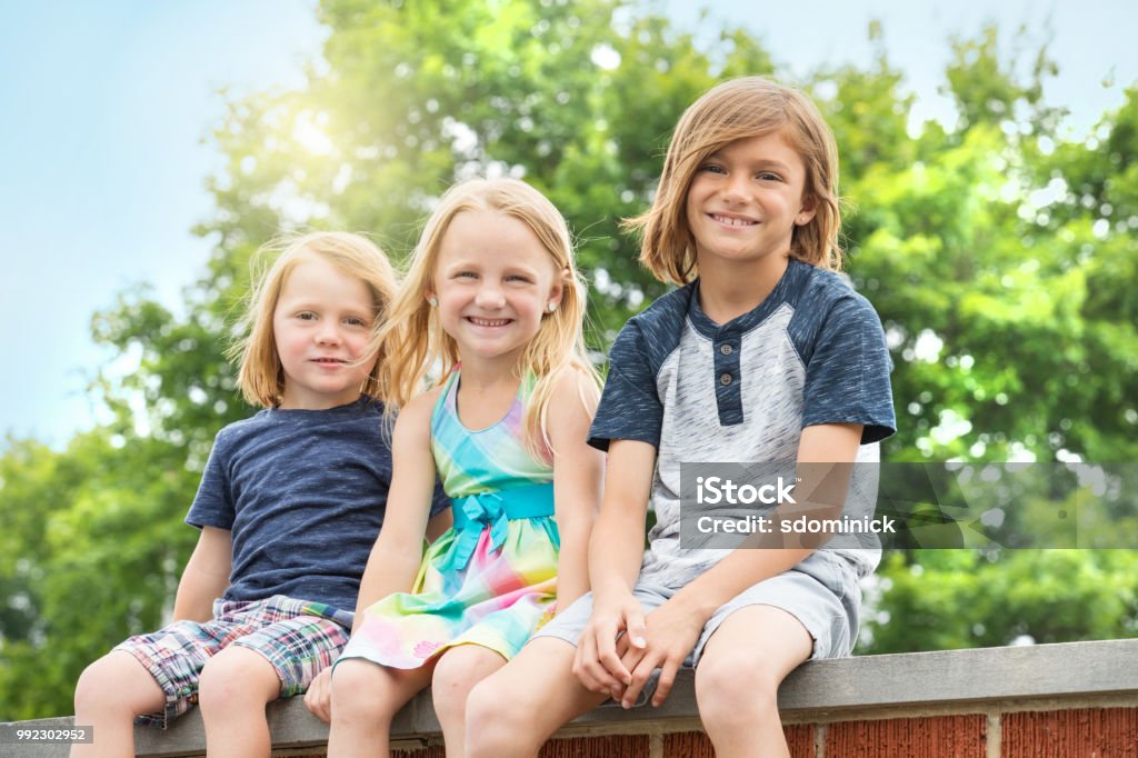 Brothers and Sister Outdoors An 8 year old brother sitting outdoors with this 6 years old sister and 3 years old brother. Blond Hair Stock Photo