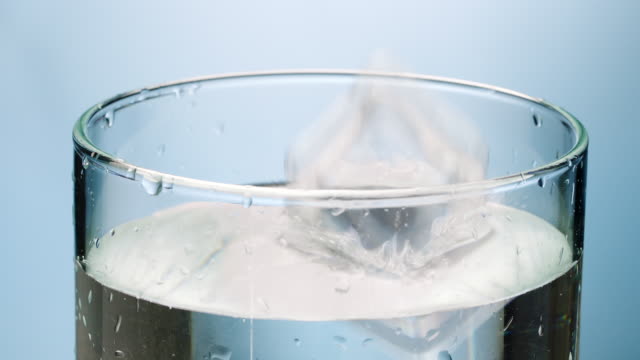 Ice cube and lemon slice falling in water glass