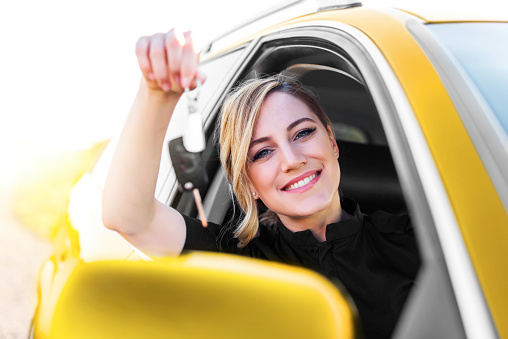 An attractive woman in the yellow car holds a car key in her hand. Rent or purchase of auto - concept.