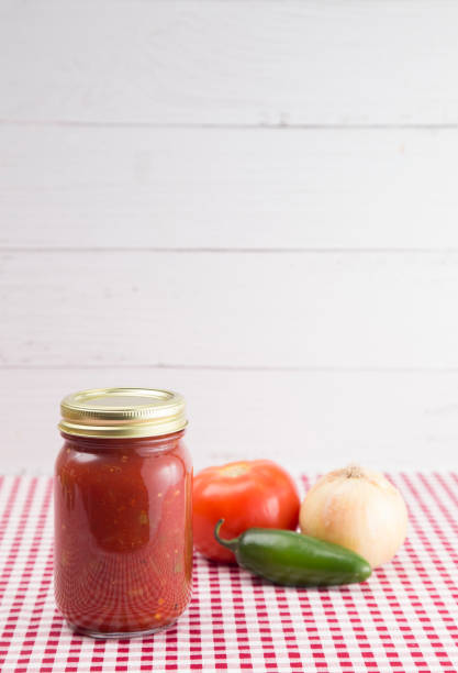 istock Salsa on a Red Gingham Table Cloth in a Home Canning Jar 992337752