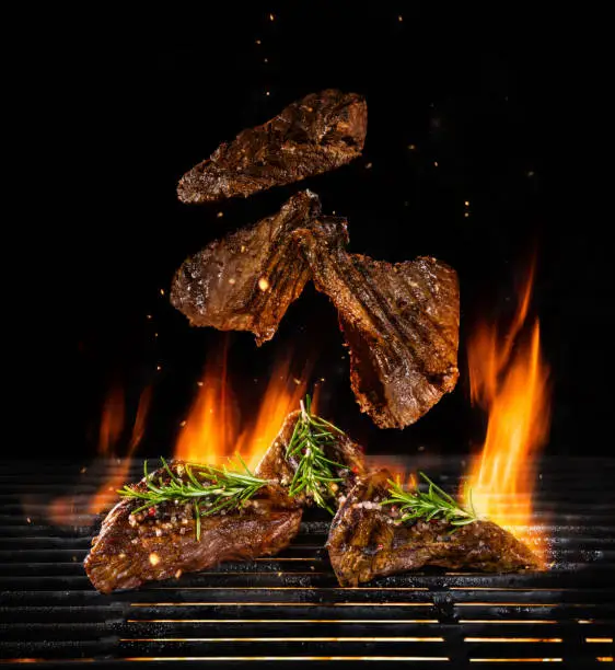 Flying beef steaks on grill with Fire flames. Isolated on black background. Barbecue and grilling. Very high resolution image