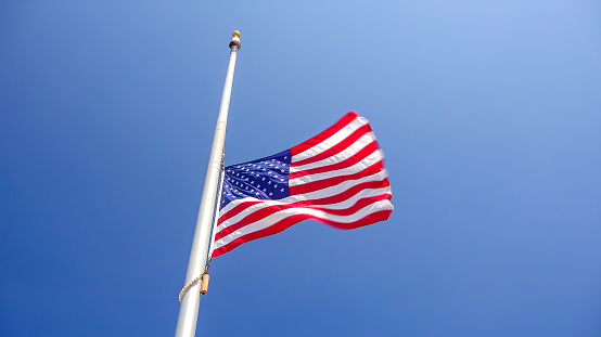 American flag flying at half mast aka half staff against a clear blue sky