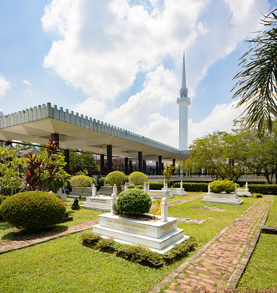 Kuala Lumpur National Mosque side view with palm trees and minaret above and a partly cloudy sky.