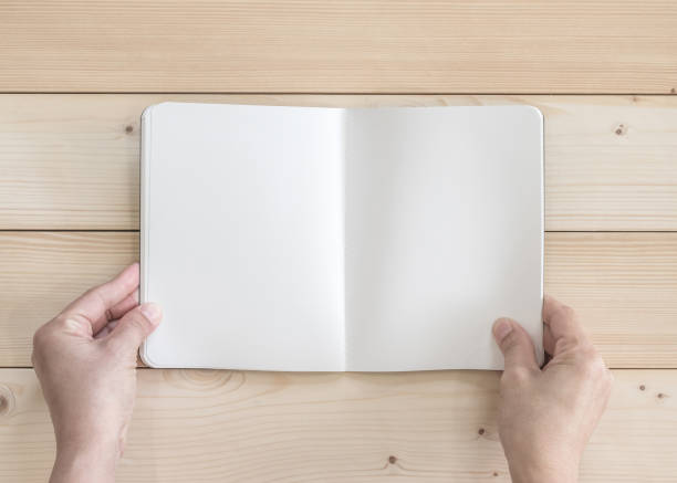 istock Blank open pocket book mock up, catalog magazines, or note template with paper texture copyspace in person's hands on white pine wood table 992442342